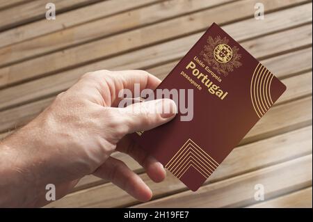 Una mano contiene un passaporto portoghese e un asse di legno sullo sfondo, spazio copia Foto Stock