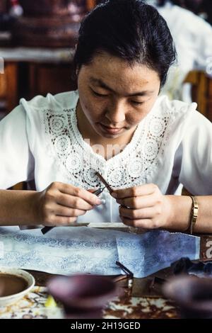 Un artigiano forma un chiodo di garofano o una striscia di filo per fare il disegno per un vaso di cloissone in un laboratorio a Pechino, Cina. Foto Stock