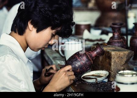 Un artigiano attacca i cloison o la striscia di filo per fare il disegno per un vaso di cloissone in un laboratorio a Pechino, Cina. Foto Stock