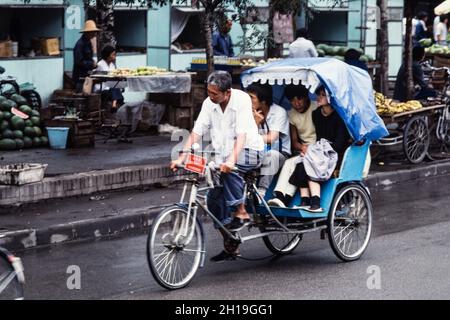 I cinesi cavalcano in un pedicab triciclo o in taxi per le strade di Pechino, Cina. Foto Stock