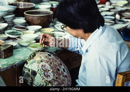 Un artigiano applica la fritta di smalto con un eyedropper su un vaso di cloissone in un laboratorio a Pechino, Cina. Foto Stock