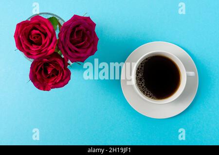 Composizione creativa di fiori di rosa rossa e tazza di caffè su sfondo blu. Concetto di molla minimo. Foto Stock