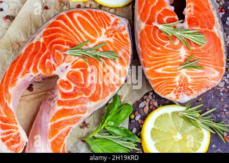 Vista dall'alto di fette di salmone rosso crudo con spezie, rosmarino e limone in cucina su sfondo chiaro. Foto Stock