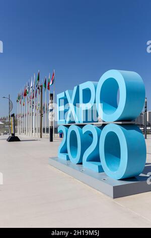 Dubai, Emirati Arabi Uniti, 17.10.2021. Expo 2020 cartello con il logo blu all'ingresso del sito dell'Expo Mobility District con bandiere nazionali dei partecipanti sullo sfondo. Foto Stock