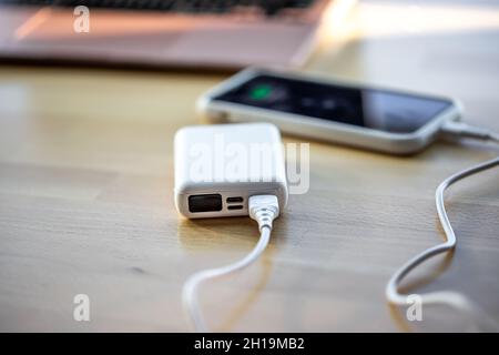Uno smartphone viene caricato da un piccolo power bank bianco. Foto Stock