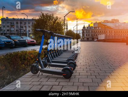 Scooter elettrici in fila sul parcheggio. Sistema di noleggio, calci scooters pubblici. Gadget tecnologici e tecnologia moderna nel settore dei trasporti. ECO concetto, ecologia cura. Trasporto alla moda. Foto Stock