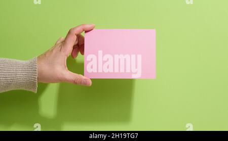 Mano femmina che tiene carta rosa vuota su sfondo verde. Copia Incolla immagine o testo, primo piano Foto Stock