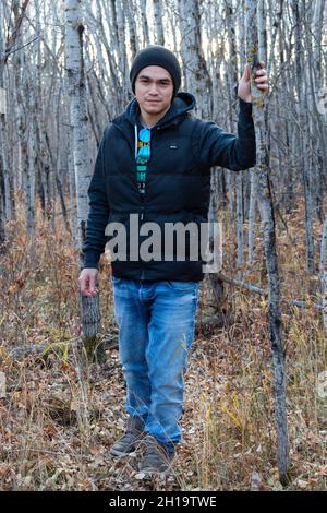 Giovane filippino uomo in piedi tra gli alberi nella foresta, camminando verso la macchina fotografica, tenendo albero per l'equilibrio Foto Stock