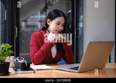 Donna d'affari che ha una videochiamata sul laptop mentre discute con il socio di affari durante il lavoro dalla sede. Foto Stock