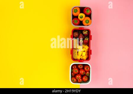 Scatole da pranzo con biscotti, pezzi di formaggio, fragole, pomodori e peperoni su sfondo colorato. Concetto di snack sano. Vista dall'alto Foto Stock