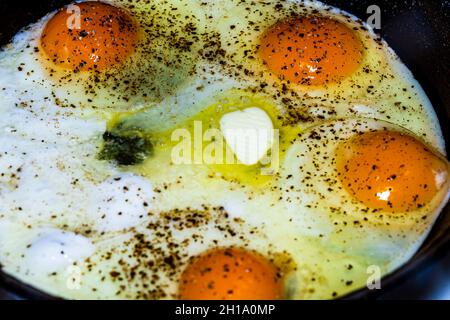 Un primo piano di quattro deliziose uova al sole con pepe nero in una pentola di cottura per la colazione Foto Stock