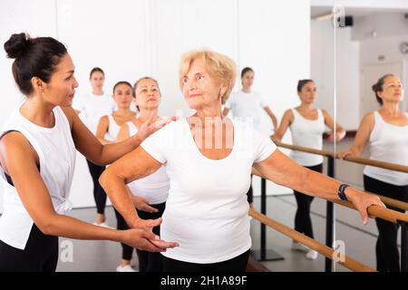 Varie donne anziane che esercitano il balletto si muove con il formatore Foto Stock