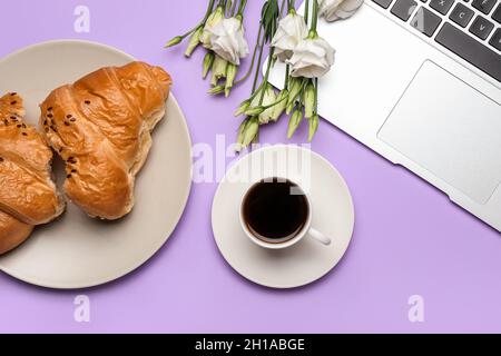 Tazza di caffè, gustoso croissant, computer portatile e fiori su sfondo colorato Foto Stock