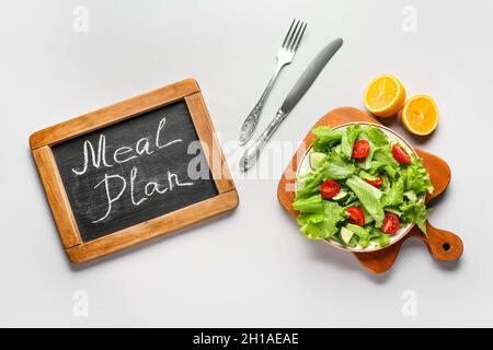 Lavagna con parole PIANO PASTO e insalata fresca su sfondo bianco Foto Stock