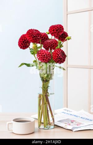 Vaso con bellissimi dahlias, giornali e una tazza di caffè sul tavolo in camera Foto Stock