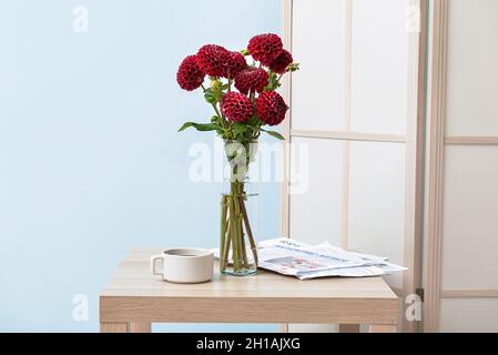 Vaso con bellissimi dahlias, giornali e una tazza di caffè sul tavolo in camera Foto Stock