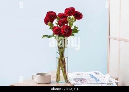 Vaso con bellissimi fiori di dahlia, giornali e una tazza di caffè sul tavolo in camera Foto Stock