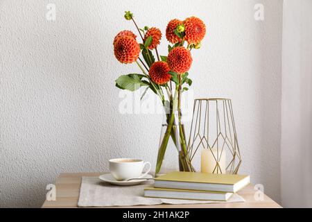 Vaso con bellissimi dahlias, libri, candela e tazza di caffè sul tavolo in camera Foto Stock