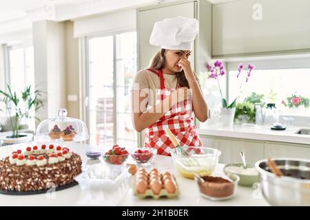 Bella giovane brunetta pasticceria chef donna cottura pasticceria in cucina odore qualcosa di stinky e disgustoso, odore intollerabile, trattenere il respiro Foto Stock