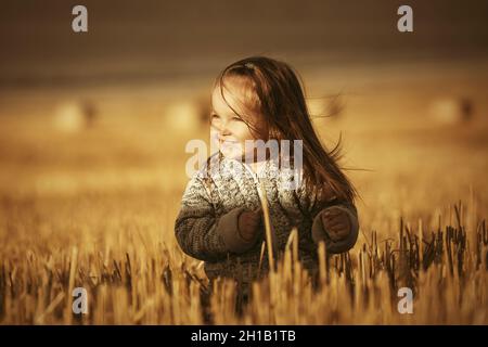 Felice ragazza di due anni in maglia felpa con cappuccio camminare in estate campo raccolto Foto Stock