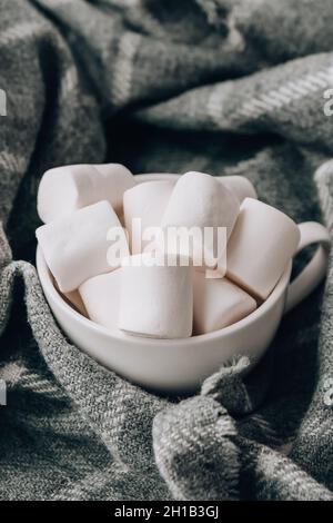 Marshmallows bianchi in una tazza bianca su sfondo maglione. Calda bevanda invernale al cioccolato cacao. Luci di Natale. Preparazione accogliente per l'atmosfera di vacanza, Foto Stock