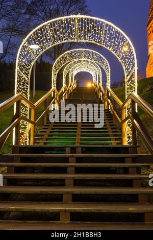 Illuminazione notturna di festa su una collina con lunghe scale di legno decorate con luci per Natale. Foto Stock