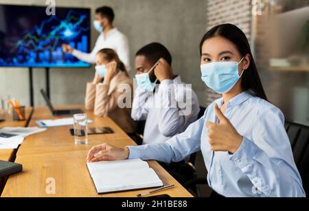 Nuova normale al lavoro. Uomini d'affari che indossano maschere mediche alla riunione aziendale Foto Stock