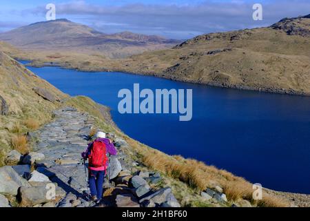 Una donna con uno zaino rosso che scende lungo la pista dei minatori a Snowdonia in una fresca giornata invernale. Foto Stock