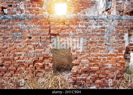 Antico muro esterno in mattoni rossi in rovina con finestra e buco Foto Stock