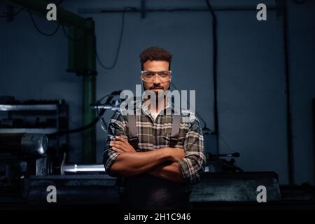 Ritratto di giovane uomo industriale che lavora in ambienti interni in officina metallica, guardando la macchina fotografica. Foto Stock