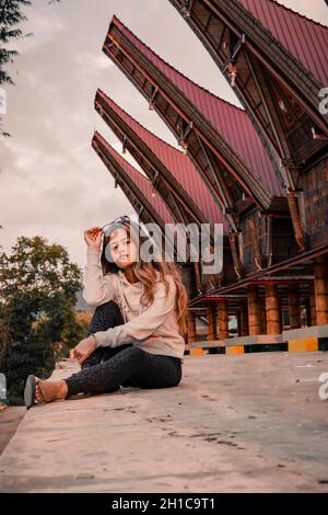 Colpo verticale di una donna indonesiana in posa in Tongkonan case tradizionali nel villaggio di Palava Foto Stock