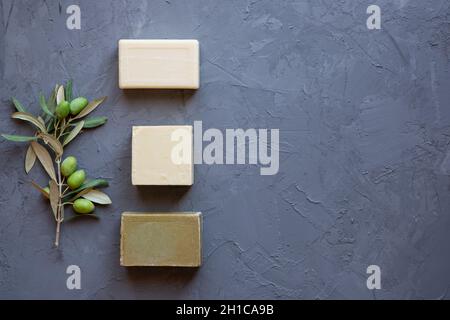 Saponette fatte a mano e ramo di oliva su sfondo grigio, trattamento di bellezza, vista dall'alto spazio copia. Foto Stock