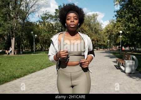 Sportivo giovane e di dimensioni più grandi con auricolari che jogging nel parco la mattina di sole Foto Stock