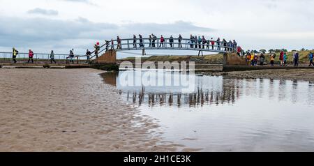 Belhaven Bay, East Lothian, Scozia, Regno Unito, 18 ottobre 2021. Pellegrinaggio del Cop26: Dopo una sosta a Dunbar, gli attivisti cristiani del clima iniziano sulla prima tappa della Via John Muir. Attraversano il Ponte fino a Nowhere e camminano attraverso la spiaggia con la bassa marea. Il pellegrinaggio si porterà a COP26 a Glasgow entro la fine del mese Foto Stock