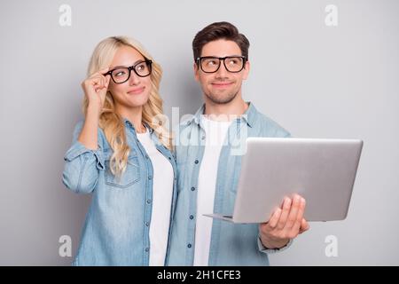 Foto di adorabile giovane coppia vestito jeans camicie occhiali in cerca di spazio vuoto tenendo gadget isolato grigio sfondo di colore Foto Stock