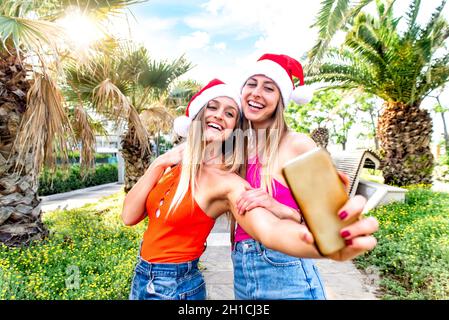 buon natale! Giovani sorelle adulte festeggiano le feste natalizie indossando un cappello babbo natale facendo un ritratto selfie all'aperto durante le calde vacanze invernali. Femmine Foto Stock