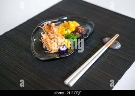 Due gamberetti in pastella con salsa e funghi sul piatto nero progettato. Gamberi fritti in legno decorato con verde e fiori Foto Stock