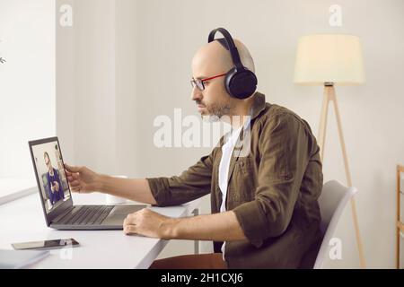Uomo in cuffie seduto di fronte al laptop a casa e in riunione di lavoro online Foto Stock