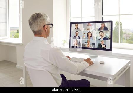 Uomo seduto alla scrivania con il computer e che tiene una riunione online con il suo team aziendale Foto Stock