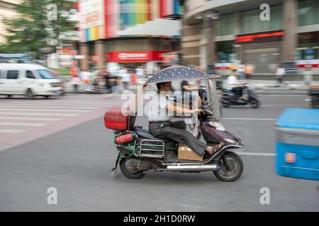 Chongqing, Cina - Agosto 2019 : uomo che guida pericolosamente veloce in uno scooter sulla strada congestionata Foto Stock