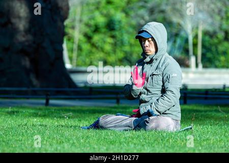 Dublino, Irlanda, Feb 2018 Signore asiatico di mezza età seduto e meditando su un prato verde in un parco verde di St Stephens, sfondo sfocato Foto Stock
