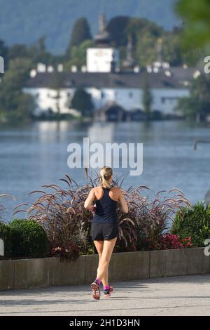 Läuferin auf der Esplanade in Gmunden mit dem Schloss Ort im Hintergrund (Bezirk Gmunden, Oberösterreich, Österreich) - Donna runner sulla spianata Foto Stock