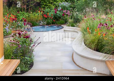 Trovare il nostro modo: Un NHS Tribute Garden. Cortile pavimentato con pavimentazione bianca e panchine in legno, piscina rialzata e aiuole fiorite. Piante includono Foto Stock