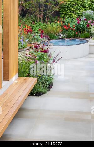 Trovare il nostro modo: Un NHS Tribute Garden. Cortile pavimentato con pavimentazione bianca e panchine in legno, piscina rialzata e aiuole fiorite. Piante includono Foto Stock