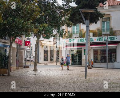 Una coppia di mezza età tiene le mani, camminando attraverso la piazza principale della città vecchia, Albufeira, Algarve, Portogallo Foto Stock