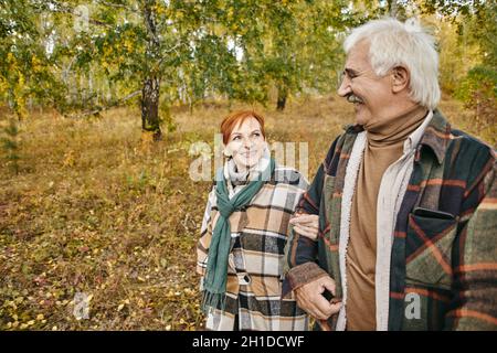 Coppia anziana felice che camminano insieme nella foresta d'autunno, parlano e si godono a vicenda Foto Stock