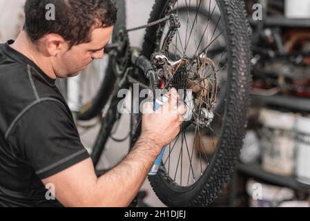Mechanic man mano, spruzzare dell'olio ad una catena di bicicletta. Manutenzione di biciclette . Foto Stock