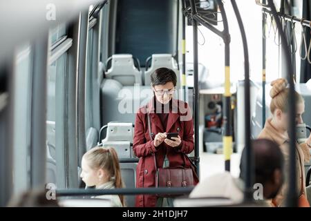 Visualizzazione ad angolo elevato per le donne adulte utilizzando lo smartphone in autobus mentre si viaggia con i mezzi pubblici in città, spazio per le copie Foto Stock