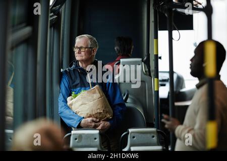 Ritratto di uomo anziano con capelli bianchi che guarda la finestra in autobus mentre si viaggia con i mezzi pubblici in città, spazio copia Foto Stock