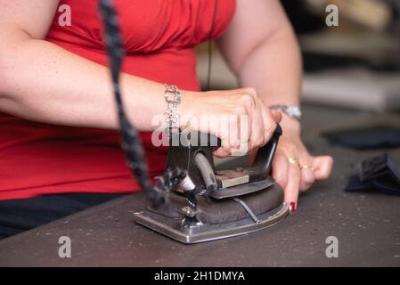 Close up di un irriconoscibile adattare la stiratura di panni con vecchio ferro metallico in un tradizionale atelier studio . Foto Stock